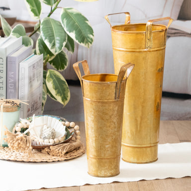 Two gold metal vases with handles on a table with a blurred background