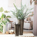 Decorative metal vases with greenery on a table in a living room setting.